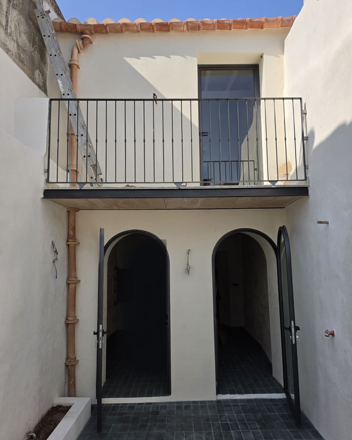 Patio de una casa de pueblo reformada en Sineu: fachada enfoscada, cubierta de teja árabe y balcón con barandilla nueva
